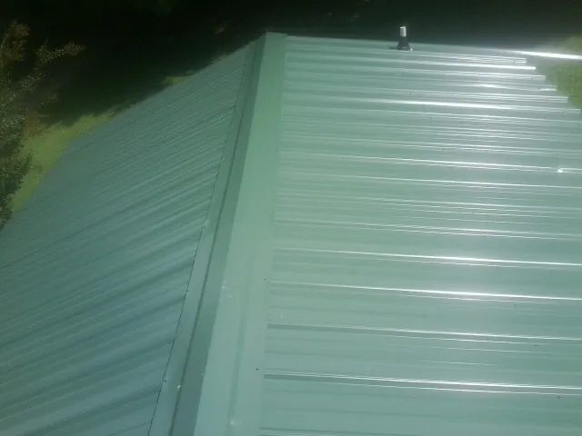 New green metal panels meeting at the ridge of a roof — Flat Roof Repair work by our crew in Youngsville